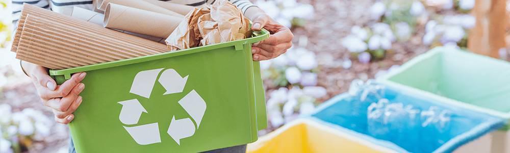 Woman holding a green recycling bx containing cardboard paper and other recyclable materials